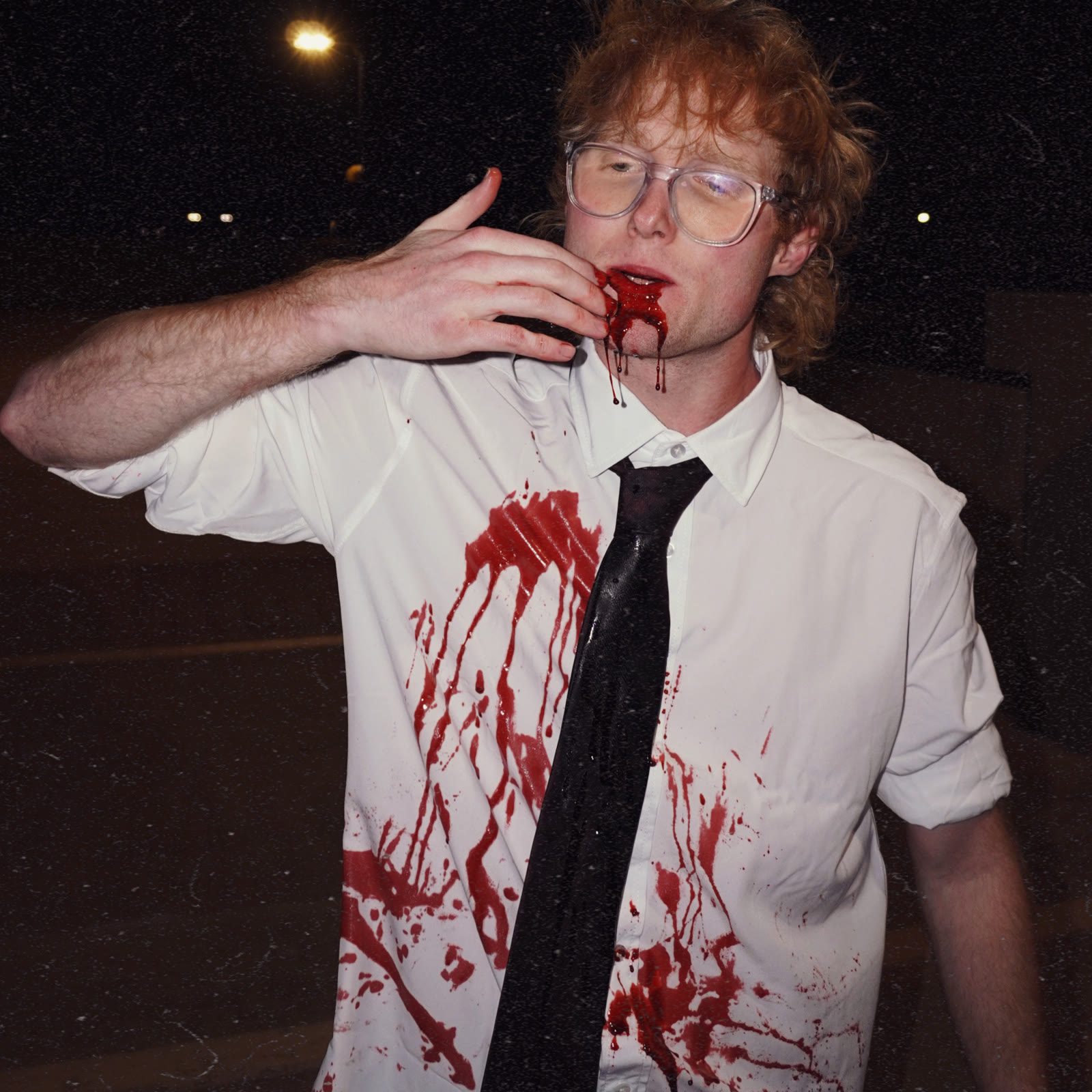 Hank Harris at night in a white shirt and black tie, fake blood running from his mouth down the shirt.